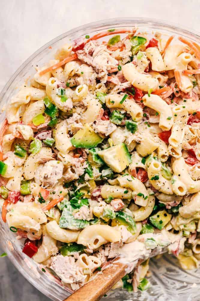 Close up of Tuna Avocado Macaroni Salad in a clear bowl with a wooden spoon for serving. 