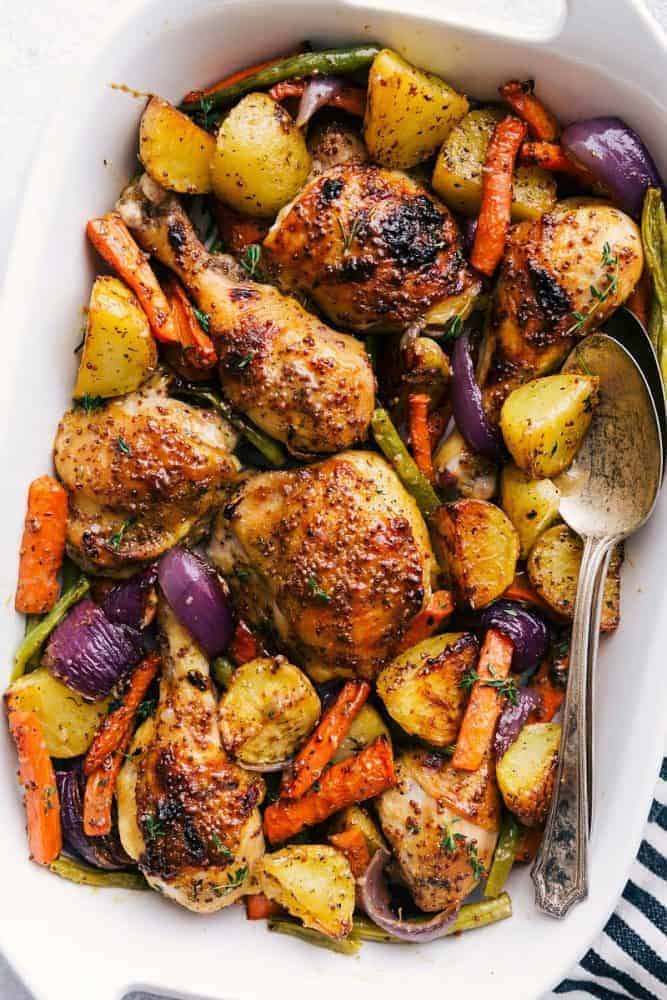 Honey Mustard Chicken and root vegetables in a white serving bowl with metal spoon. 