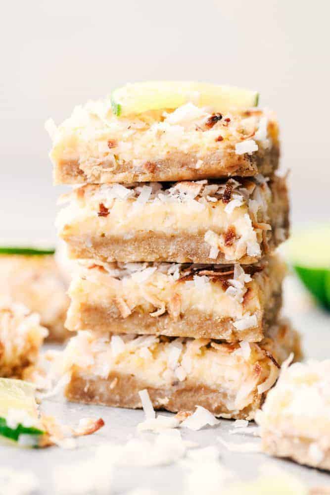 Four Coconut Lime Butter Bars stacked on top of each other with a fresh sliced lime on top. 