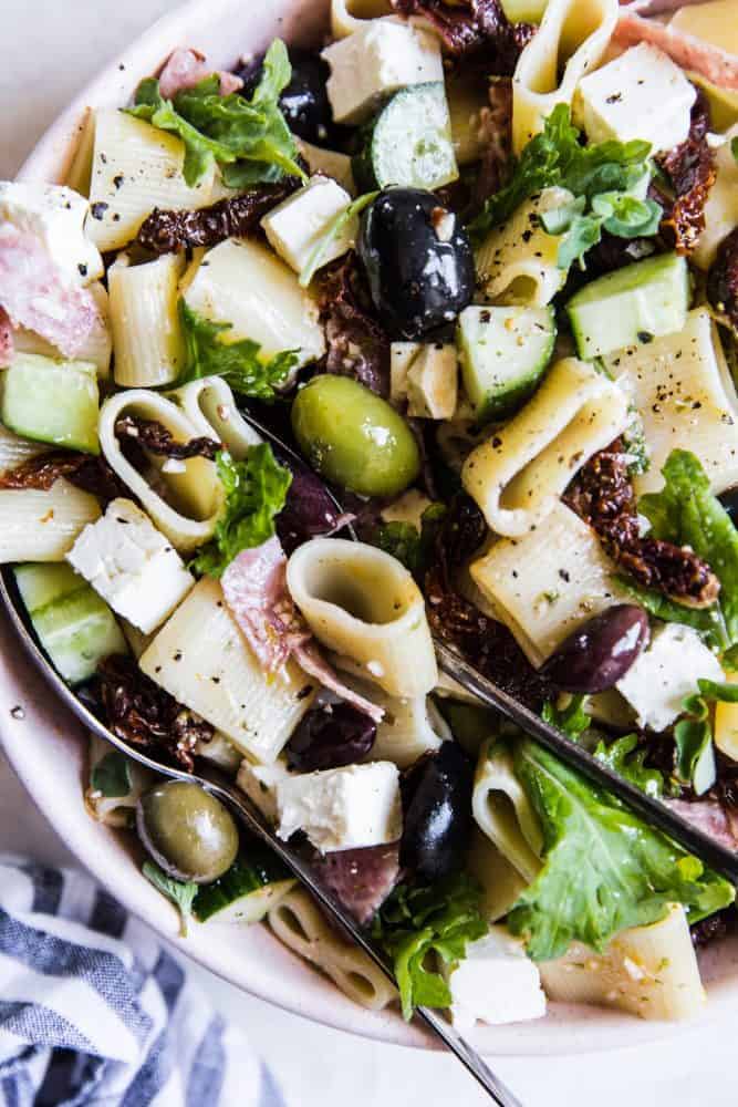 Close-up of Mediterranean Pasta Salad in a white bowl with a metal spoon. 