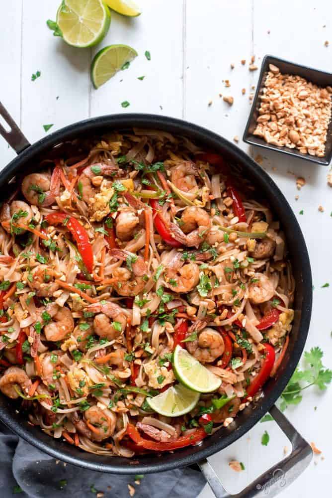 Shrimp Pad Thai in a black skillet with peanuts and sliced lime on the side. 