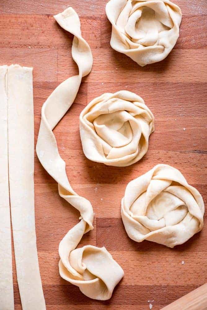 Dough being rolled into danishes on a wood table. 