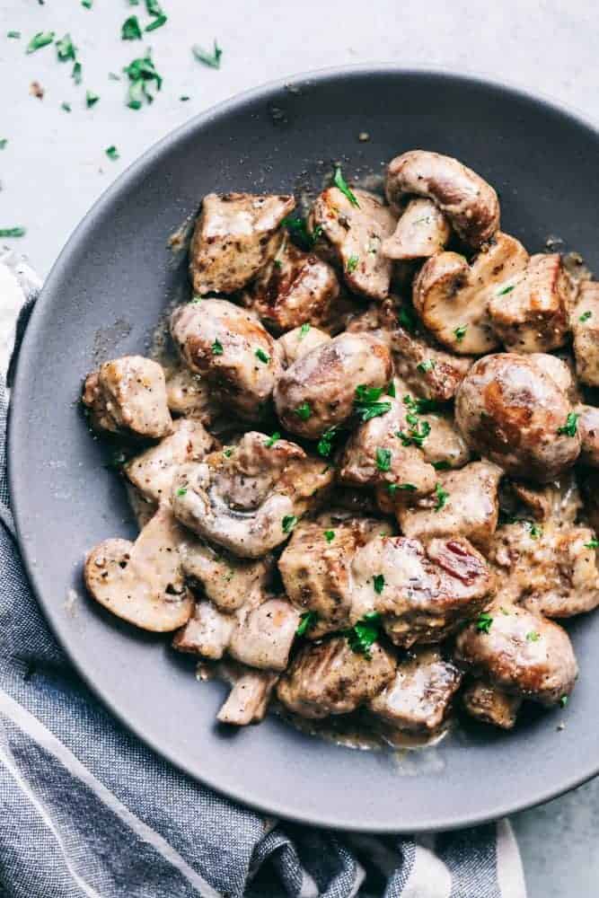 Creamy garlic steak bites with mushroom served on a gray plate garnished with fresh parsley. 