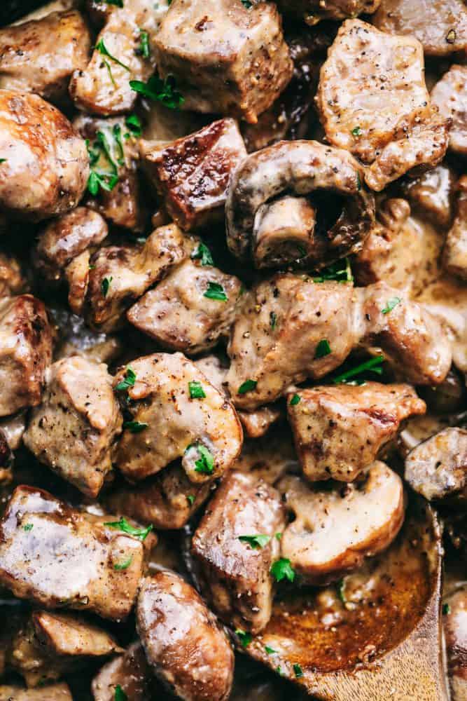 Up close photo of garlic steak bites with mushrooms and a wooden spoon in the lower right hand corner.