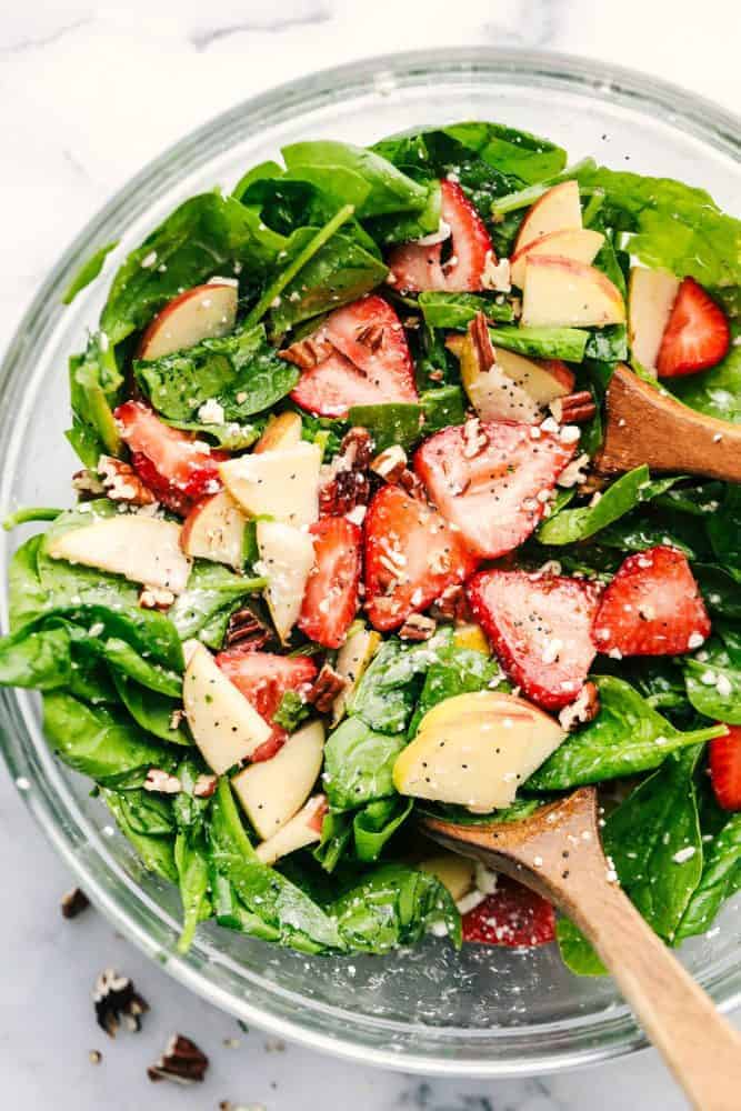 Strawberry, Apple, and Pear Spinach Salad in a clear bowl with a wooden spoon. 