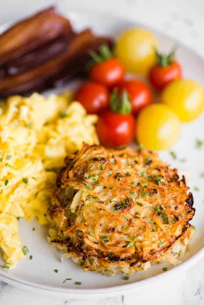 Baked Parmesan Hashbrowns on a white plate with eggs, bacon and small tomatoes. 