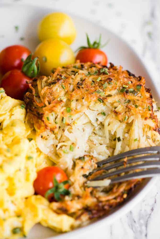 Baked Parmesan Hashbrowns on a white plate with scrambled eggs and small tomatoes. 