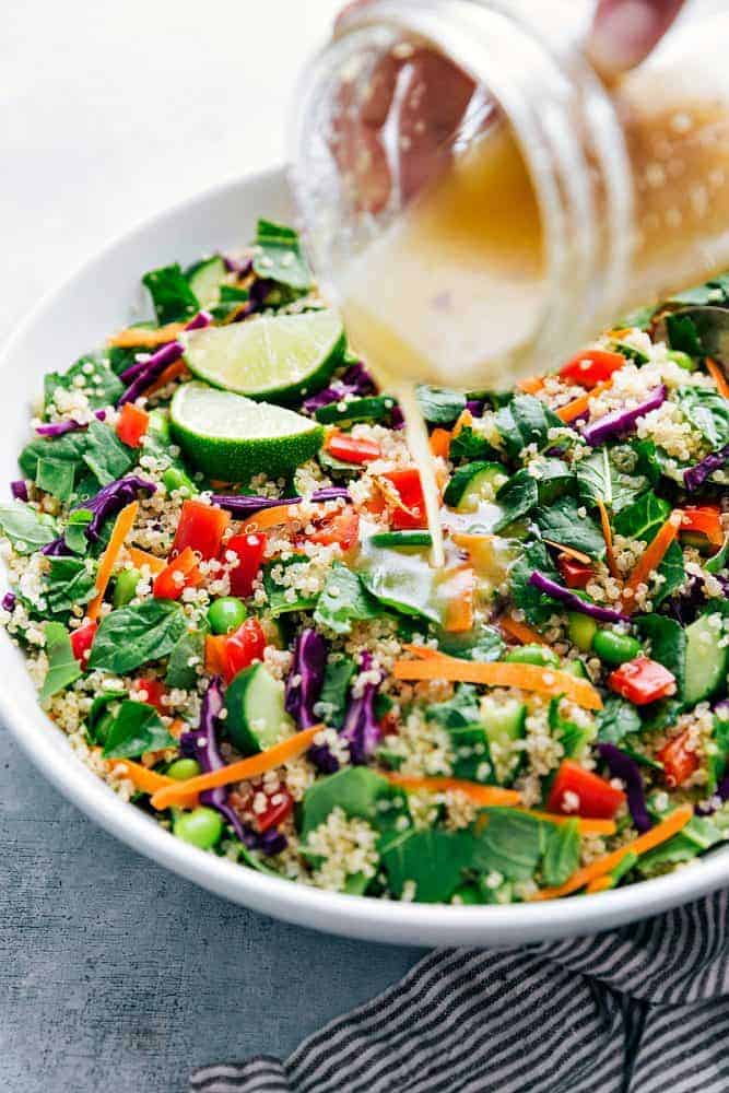 Thai quinoa salad in a white bowl with dressing being drizzled over the top. 