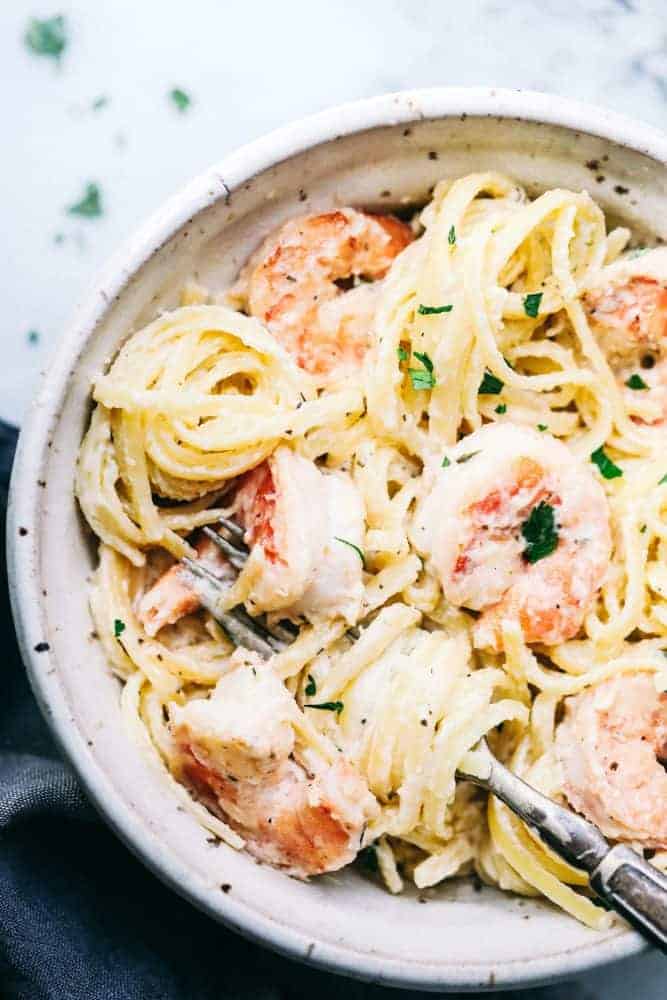 Creamy garlic shrimp Alfredo pasta in a white bowl with a fork in the bowl.