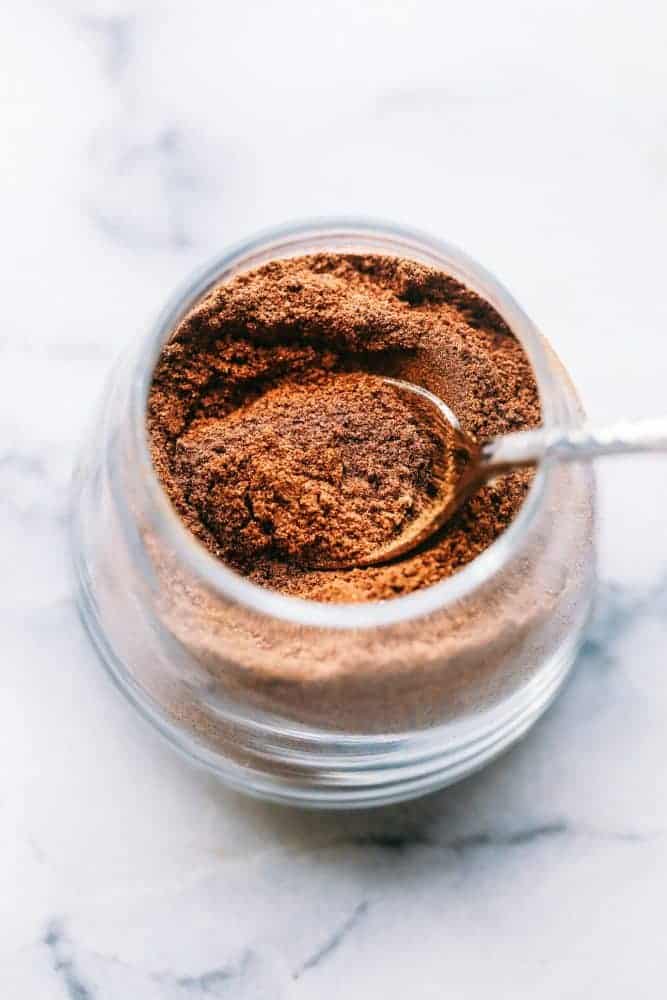 Spices in a clear glass jar with a metal spoon. 