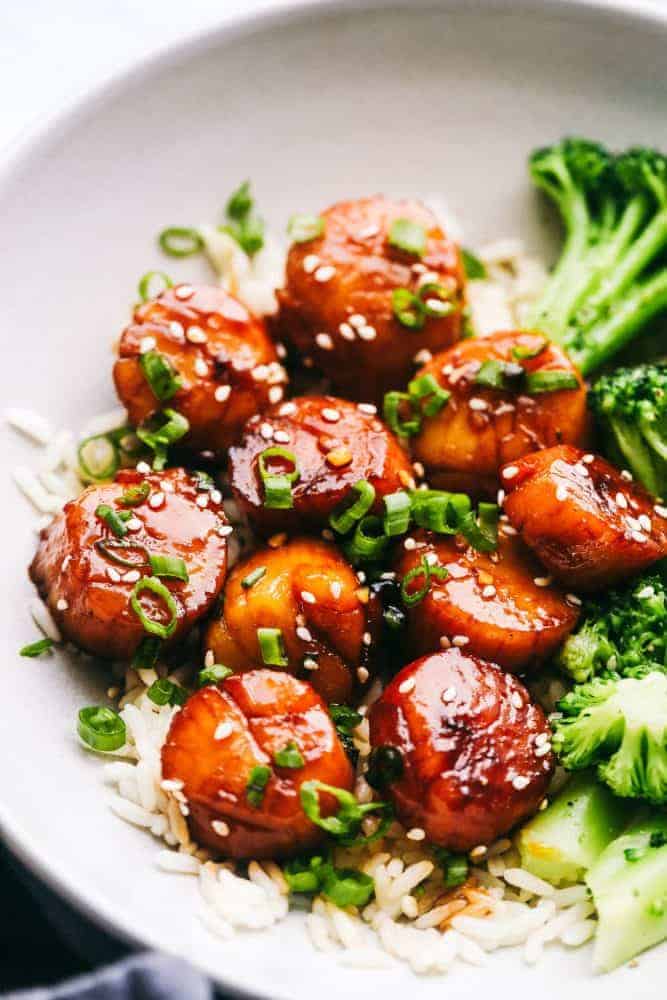 Honey Garlic Butter Scallops over white rice in a white bowl with broccoli on the side. 