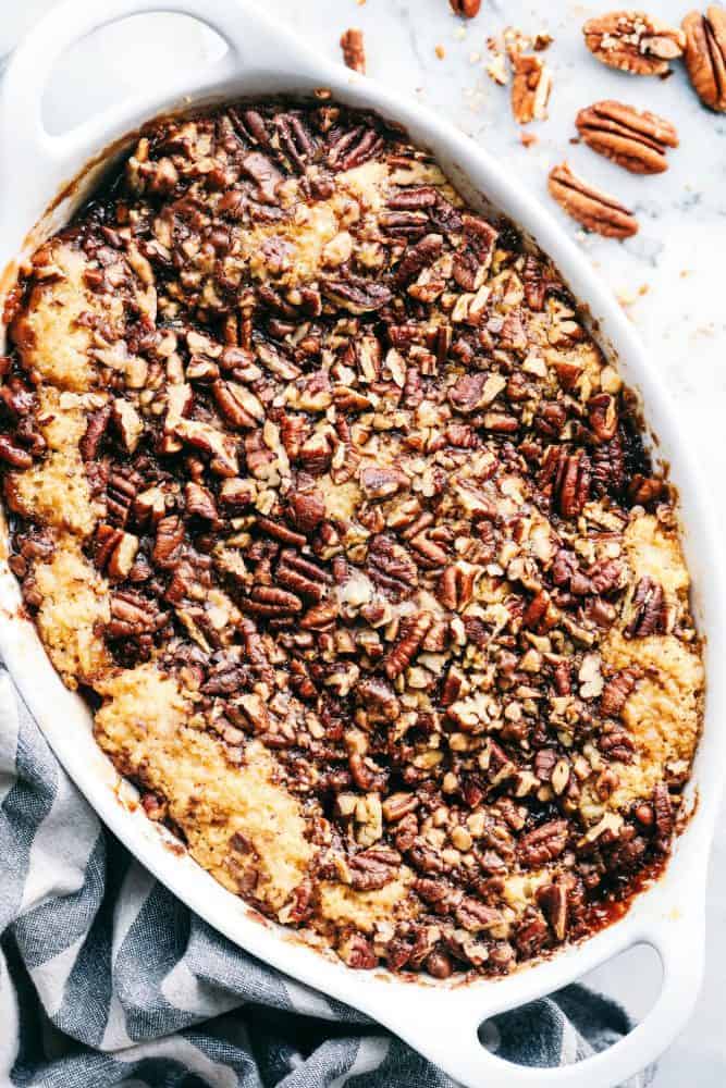 Overhead view of Pecan Pie Cobbler in a white dish with pecans on the table next to the dish. 