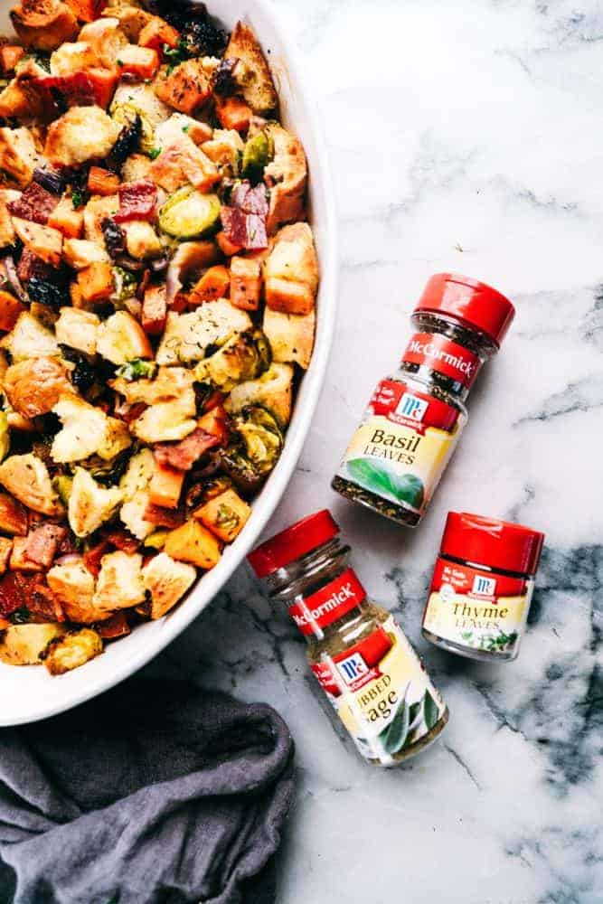 Roasted autumn vegetable stuffing and a white casserole dish with McCormick seasoning's on the side are the bottles of basil leaves, sage and thyme and their bottles.