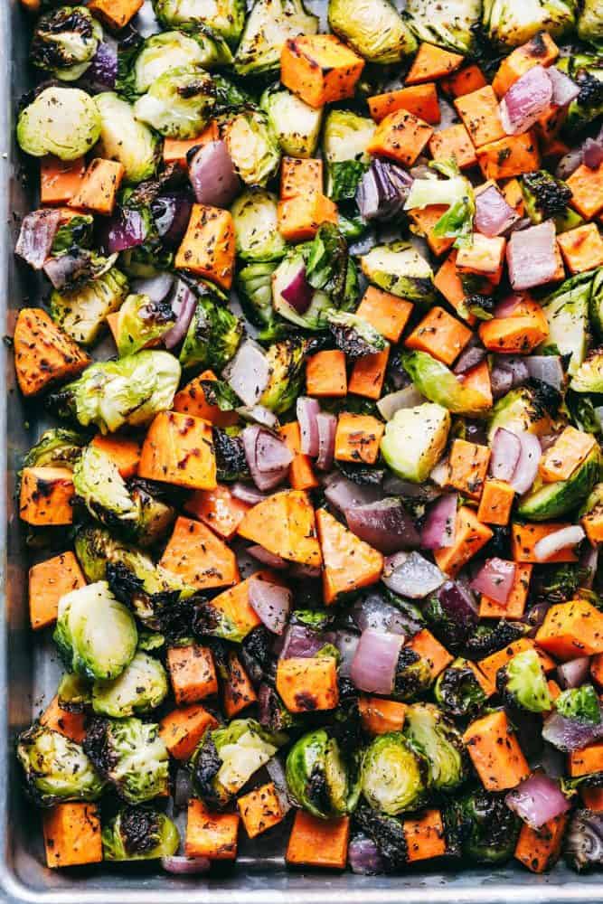 A baking sheet full of chopped up carrots, red onions and brussels sprouts with McCormick seasoning.