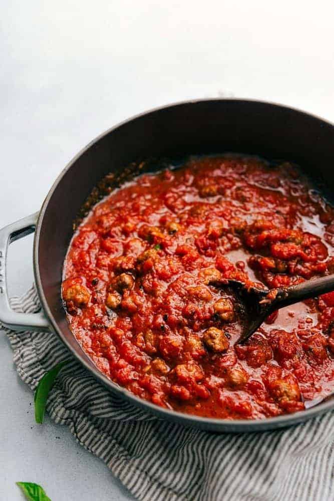 Tomato sauce being cooked any sauce pan using a wooden spoon.