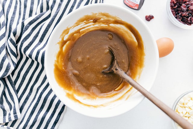 The batter of white chocolate cranberry Blondies being mixed together in a white bowl by a wooden spoon.