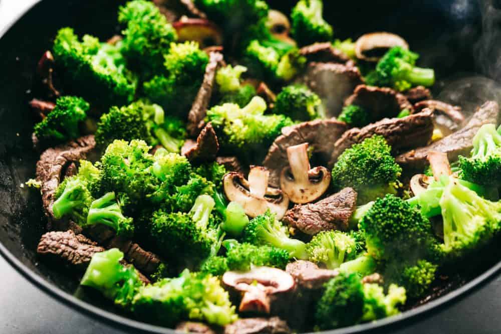 Broccoli mushrooms and garlic are being stir fried together.