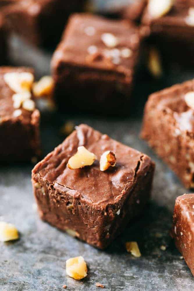 Fantasy fudge cut into 1 inch pieces garnished with walnuts over top sitting on a black countertop