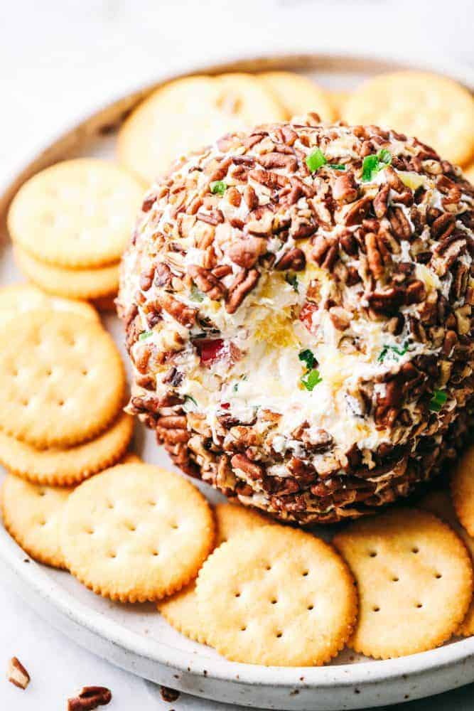 Pineapple cheese bar with a bite out of the top of it to show the pineapple and chives With Ritz crackers surrounding it served on a white plate.