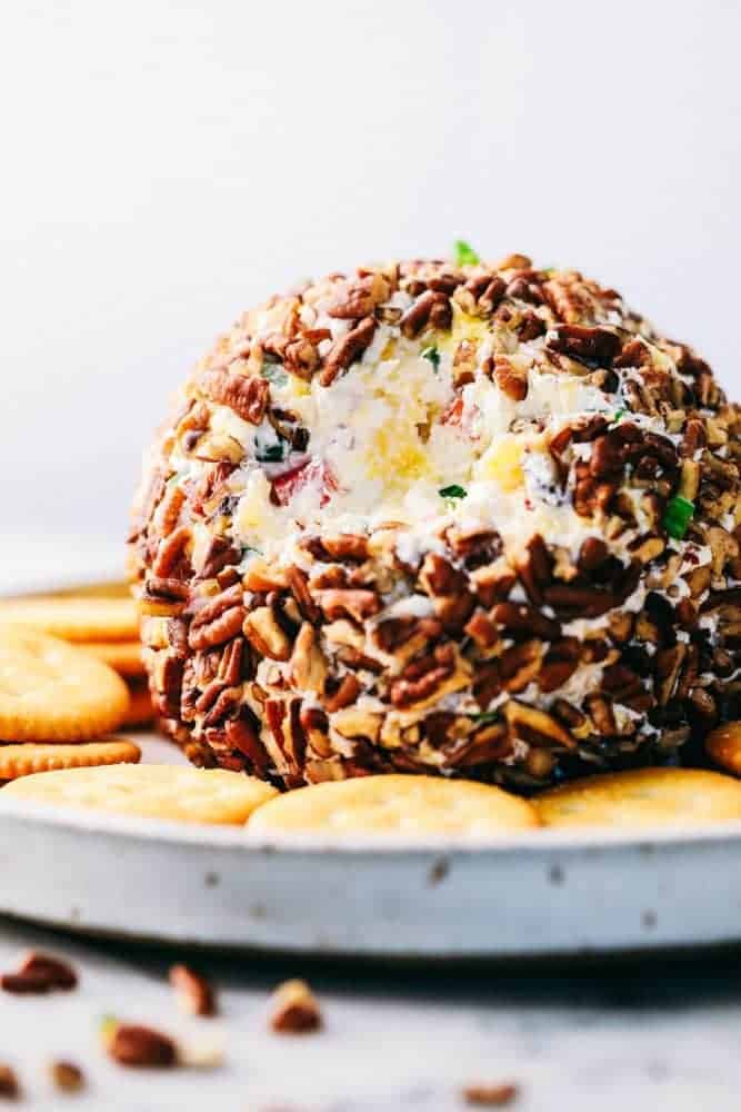 Pineapple cheese ball with crackers all around it on a white plate.