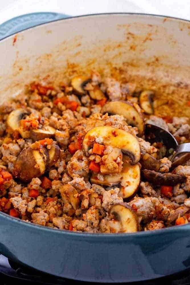 ground turkey, diced carrots and mushrooms cooking in a dutch oven