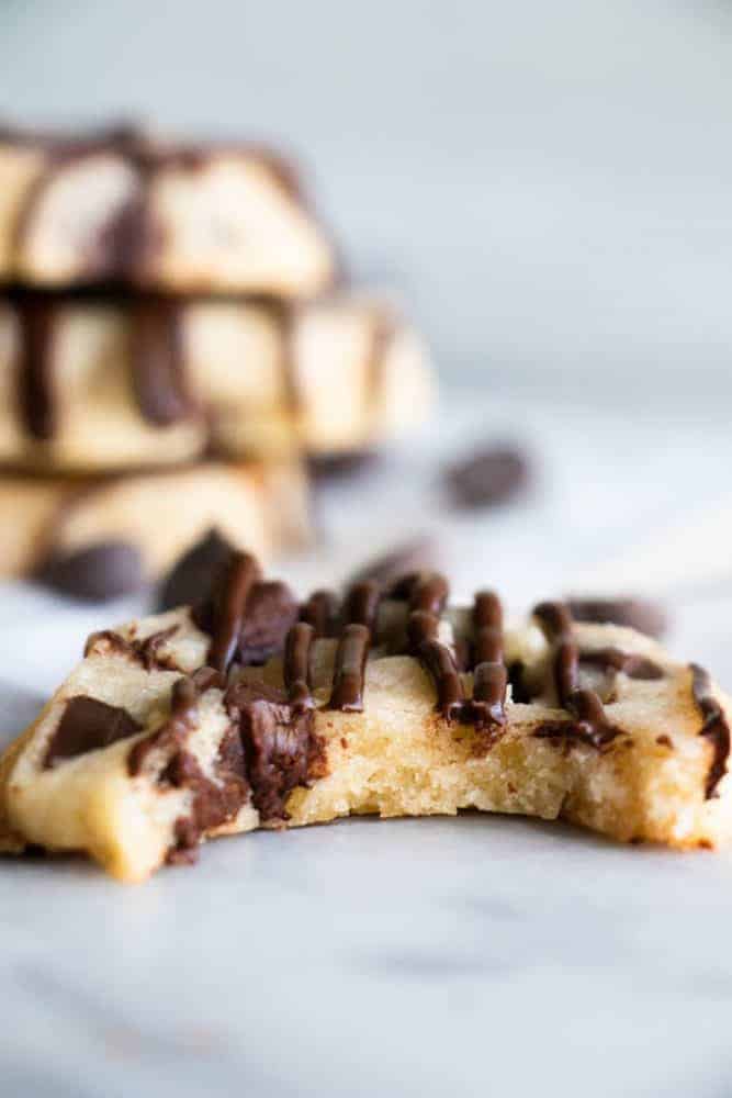 A chocolate chip shortbread cookie with a bite taken out of it and three chocolate chip shortbread cookies stacked in the background.