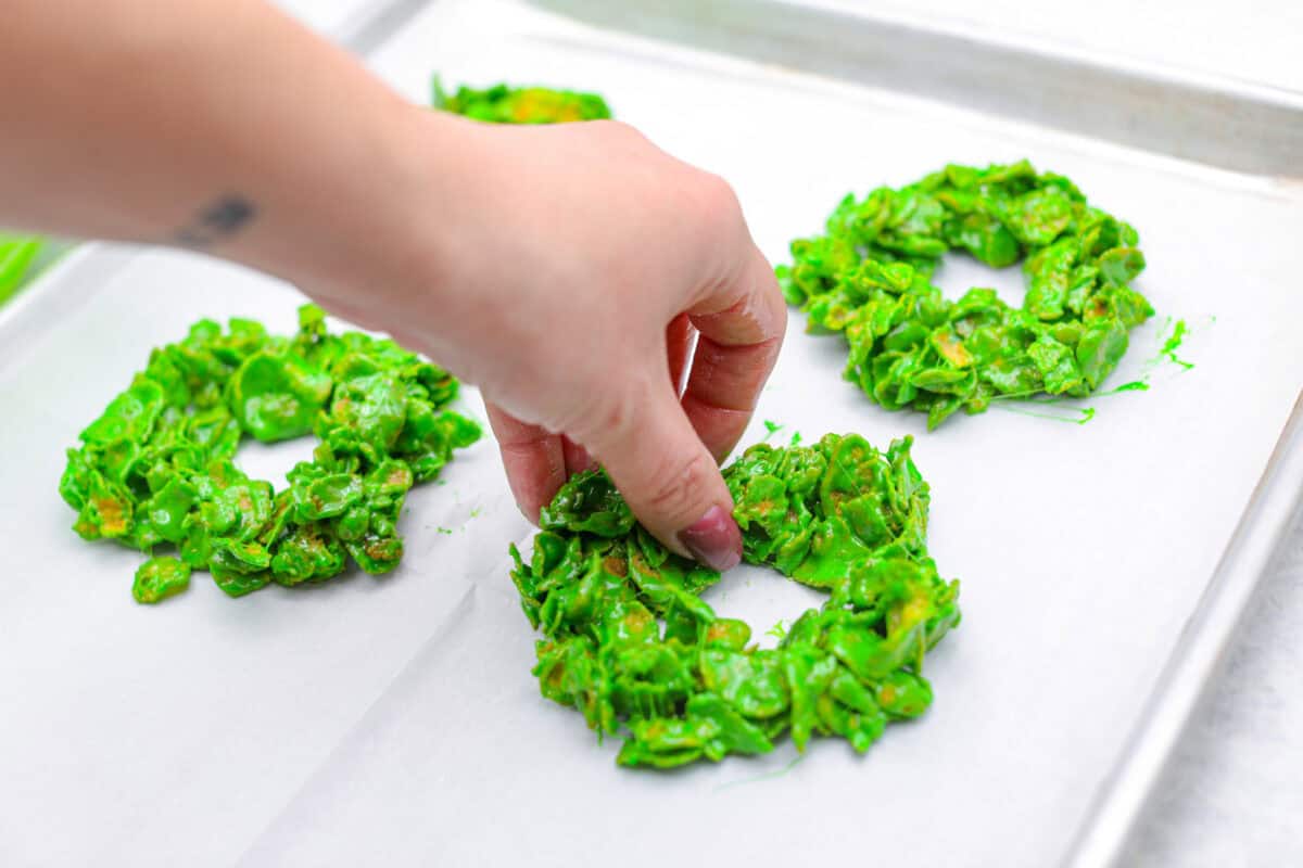 Angle shot of someone shaping the wreaths with their hands on parchment paper on a cookie sheet. 