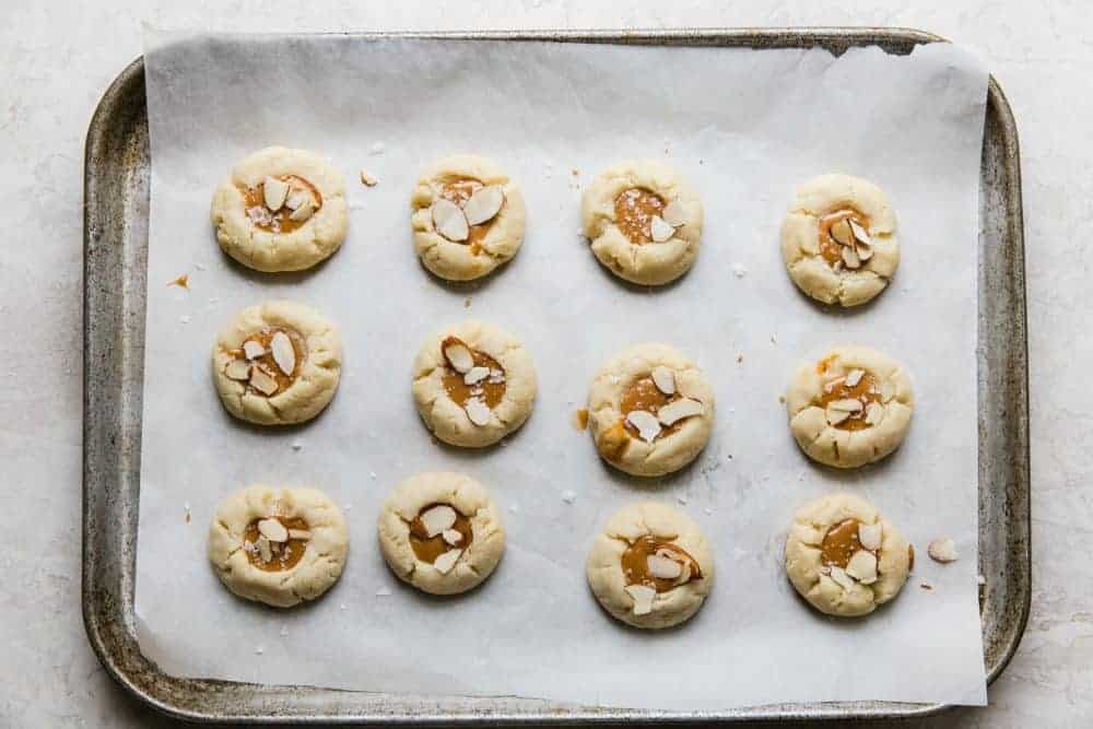 Almond thumbprint cookies on cookie sheet with salted caramel center.