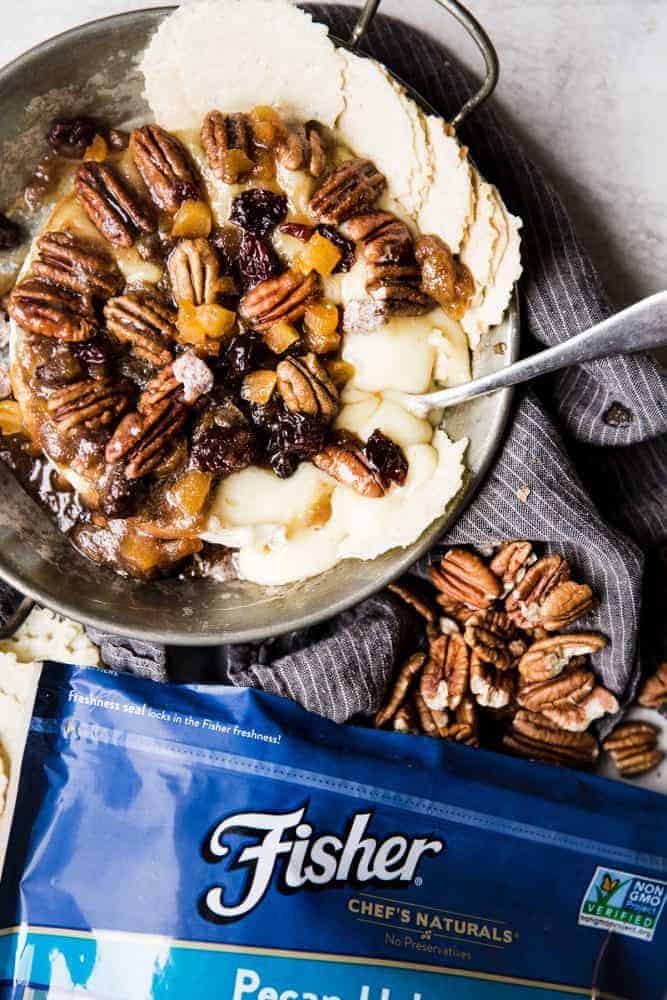 Maple pecan baked brie in a serving dish with chips on the side. There is the bag of Fishers pecan halves on the side.