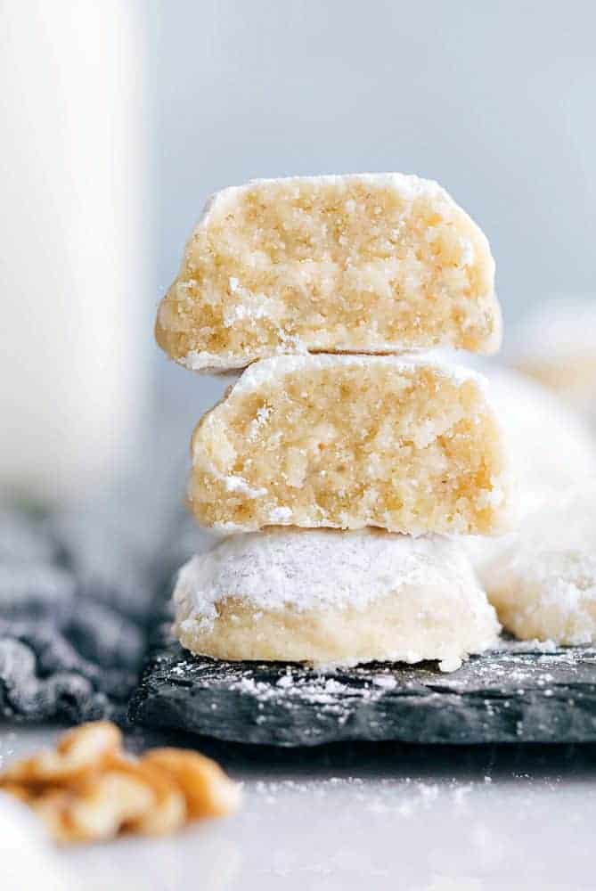 Snow kiss cookies stacked on top of one another on a black cutting board.