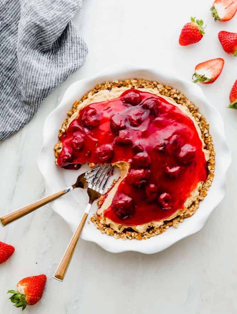 Strawberry peanut butter pie in a white pie dish with two metal forks and fresh cut strawberries on the table on the side.