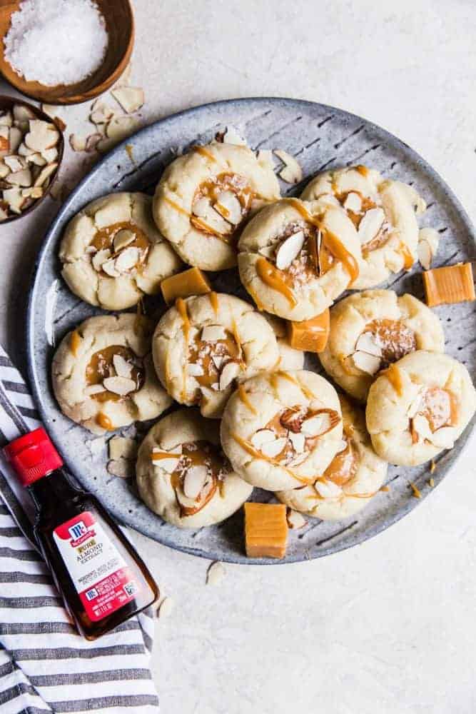 Allman thumbprint cookies on a gray plate with a small bottle of McCormick Almond extract on the side.