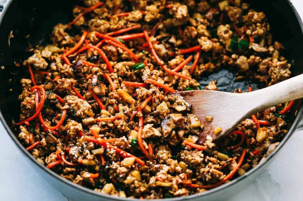 The filling for asian turkey lettuce wraps in a skillet with a wooden spoon. 