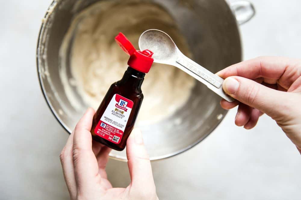 Hands measuring almond extract to be placed in with recipe.