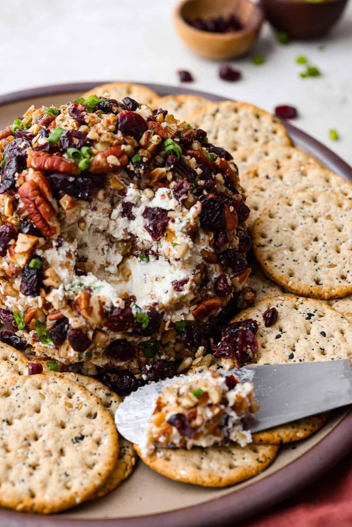 Close view of a cranberry pecan cheese ball on a platter with crackers and a knife.