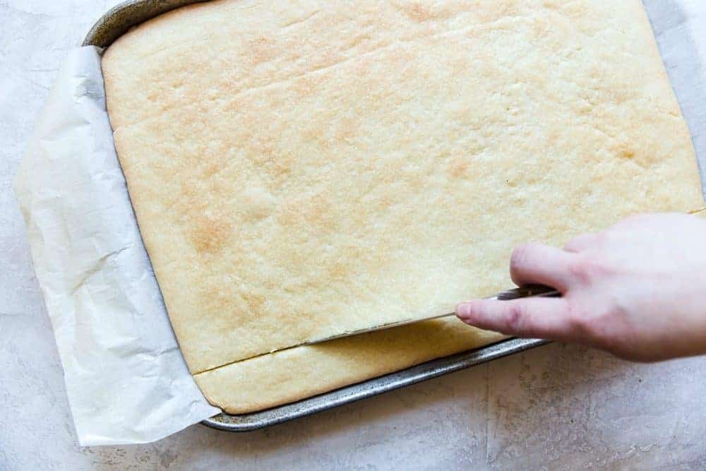 Shortbread cookies on a cookie sheet being sliced with a knife.