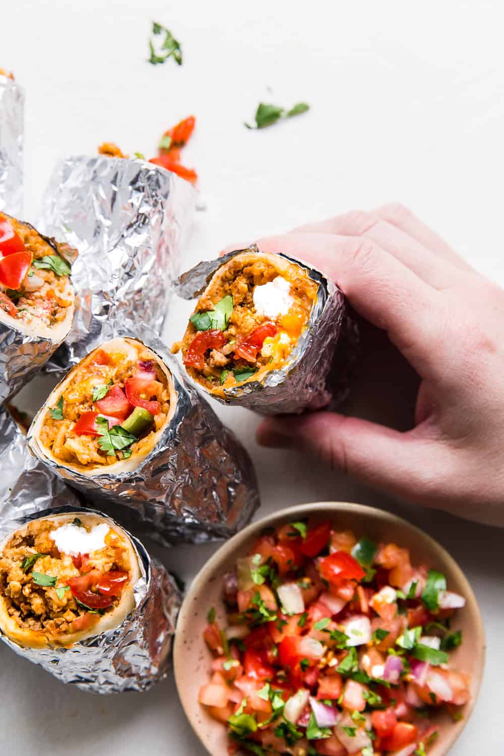 Stack of mini burritos with a brown bowl of salsa on the side.