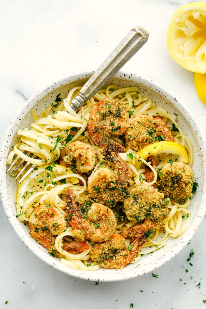 Lemon garlic shrimp in a bowl over top linguine noodles with a fork inside the bowl. 