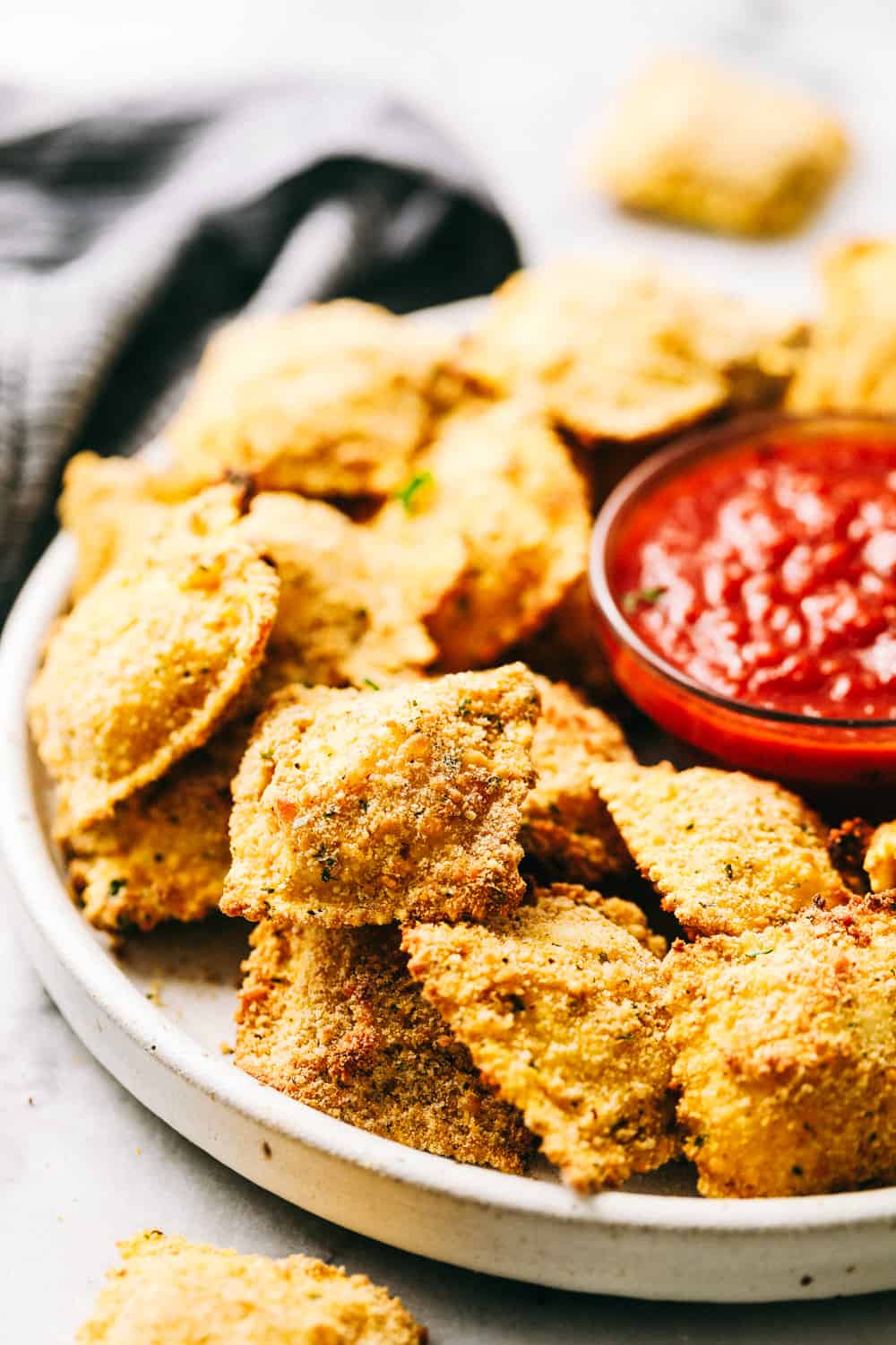 Crispy Baked Parmesan Ravioli stacked on a plate with sauce.