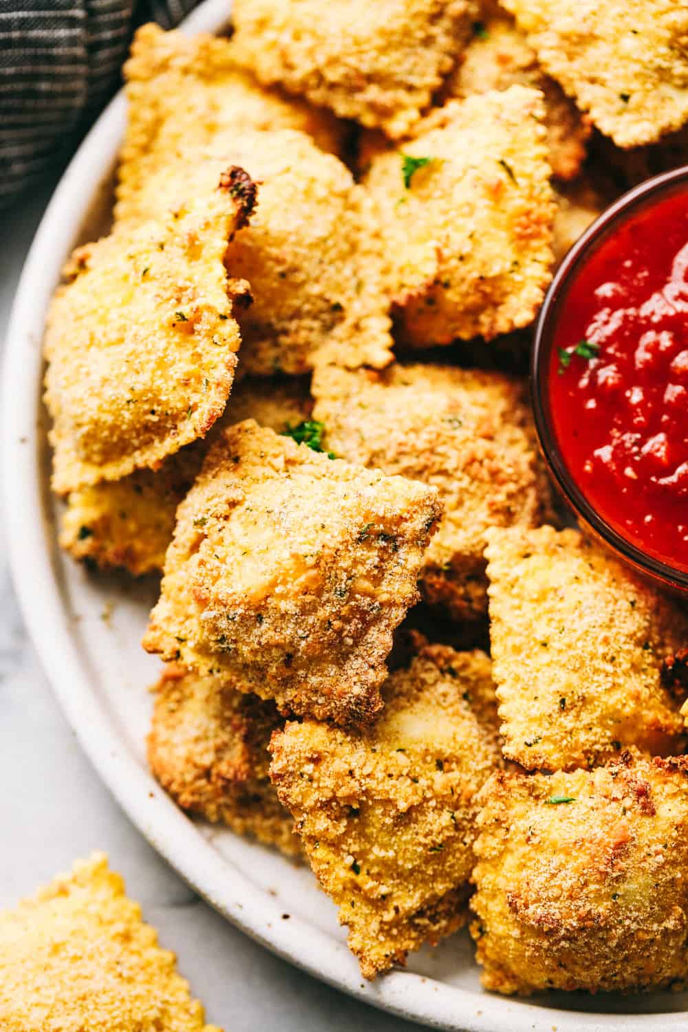 Crispy Baked Parmesan Ravioli stacked on a plate with sauce.