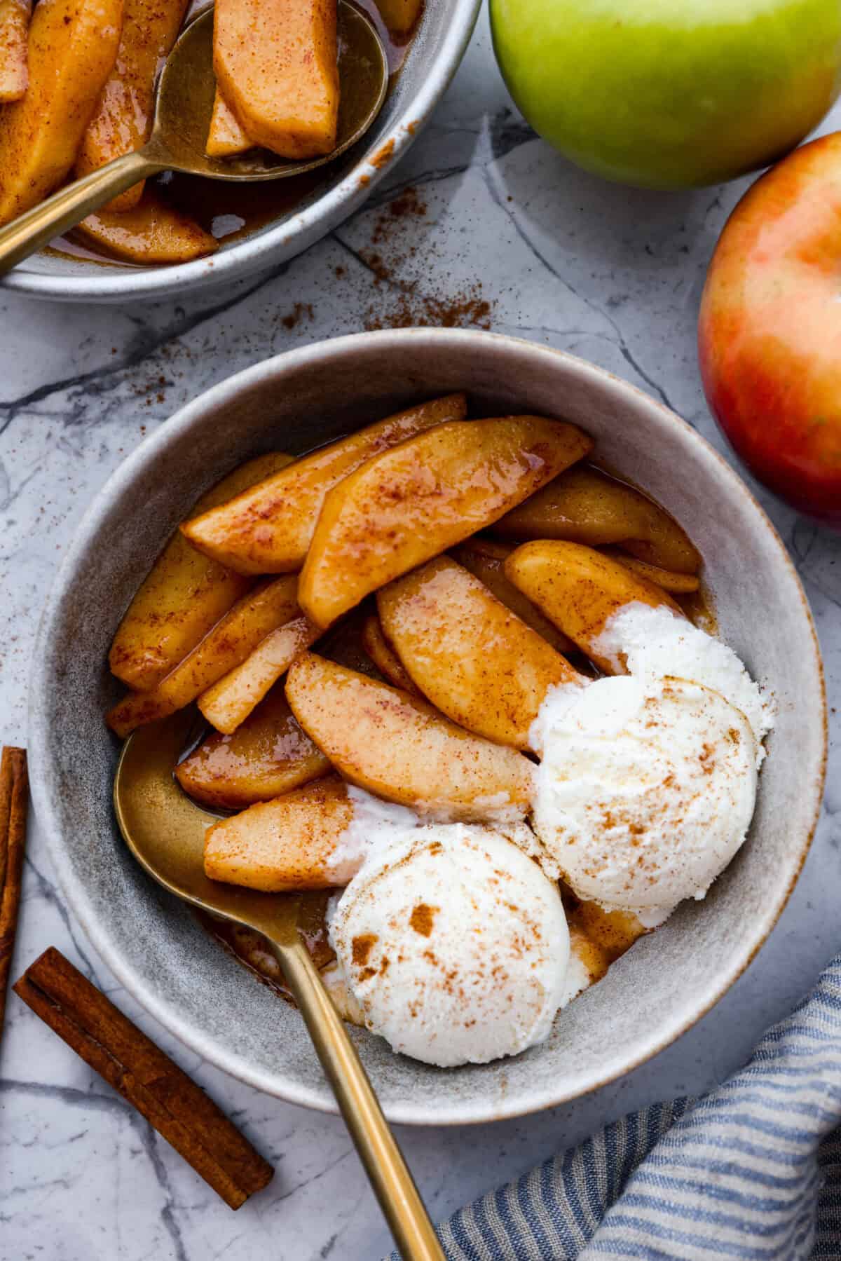 Overhead shot of serving of brown sugar and cinnamon baked apples in a bowl with two scoops of vanilla ice cream. 