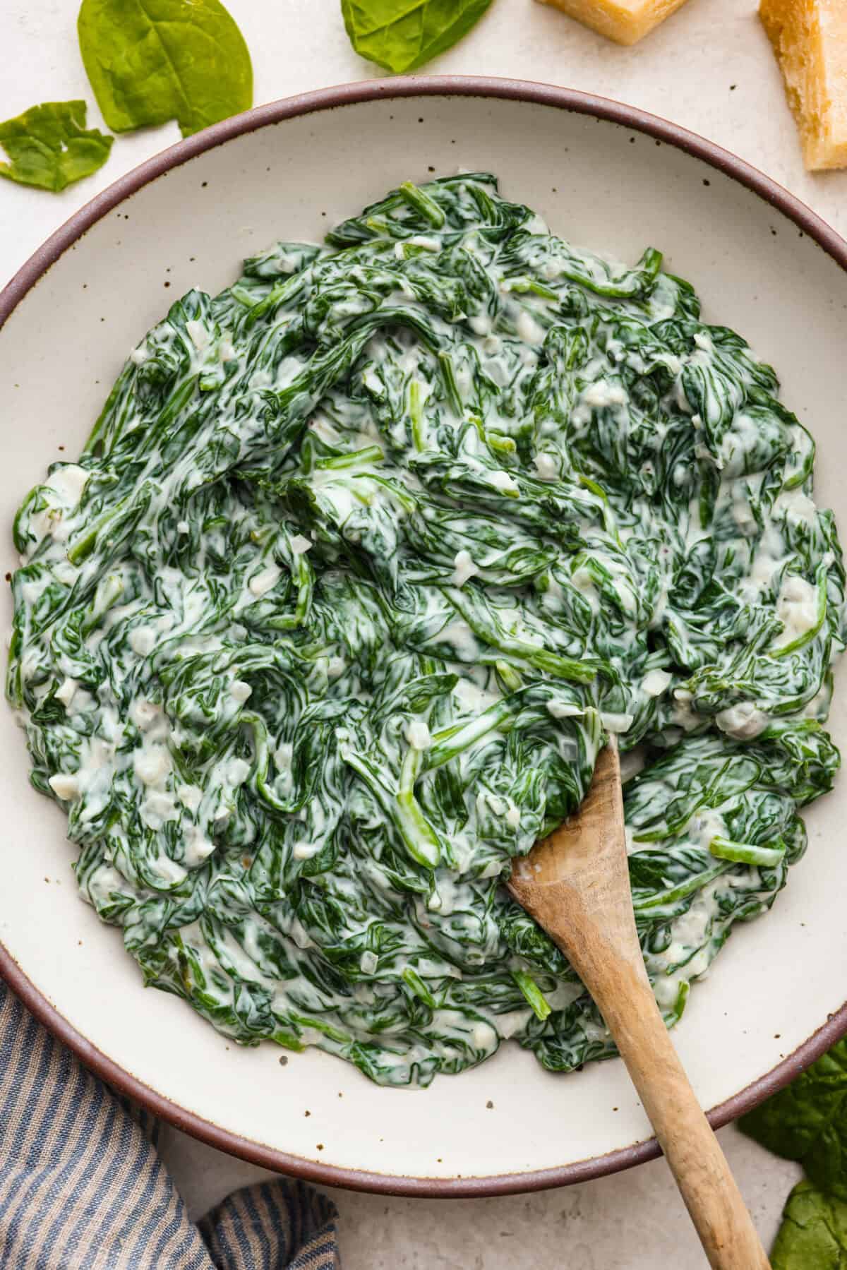 Top view of creamed spinach in a serving bowl with a wood spoon.