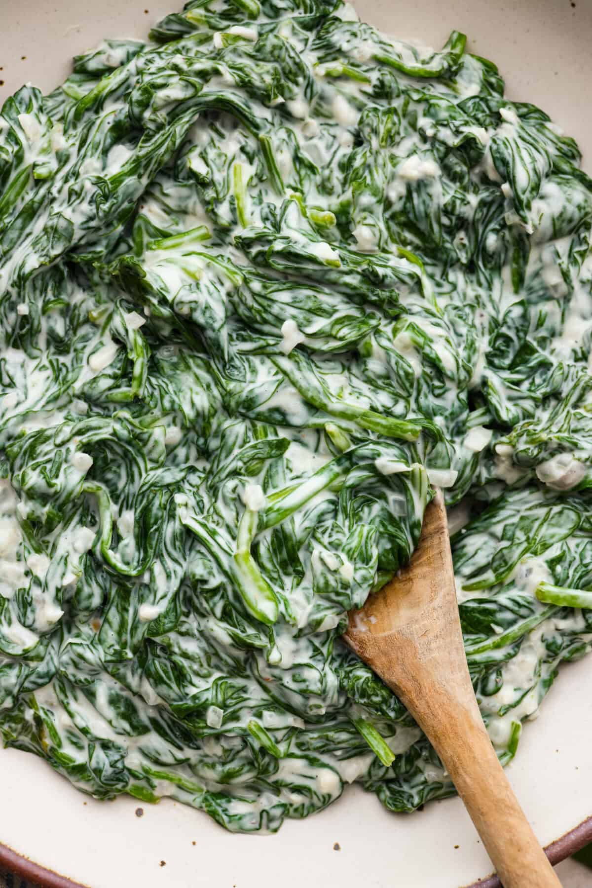 Close view of creamed spinach in a serving bowl with a wood spoon.