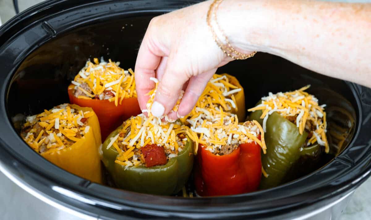 Angle shot of someone sprinkling cheese on top of bell peppers in crock pot. 