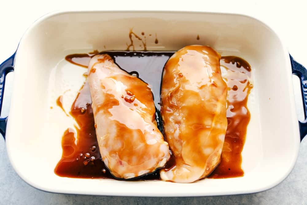 Teriyaki sauce over chicken breast in a pan getting ready to be baked. 