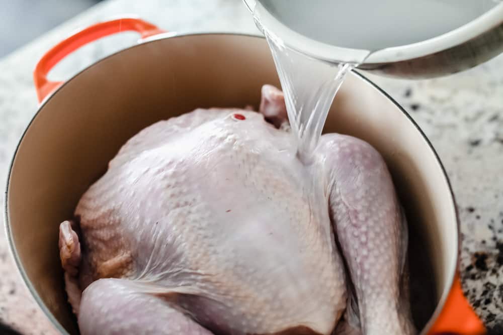 Pouring the salted water over the turkey in a pot.