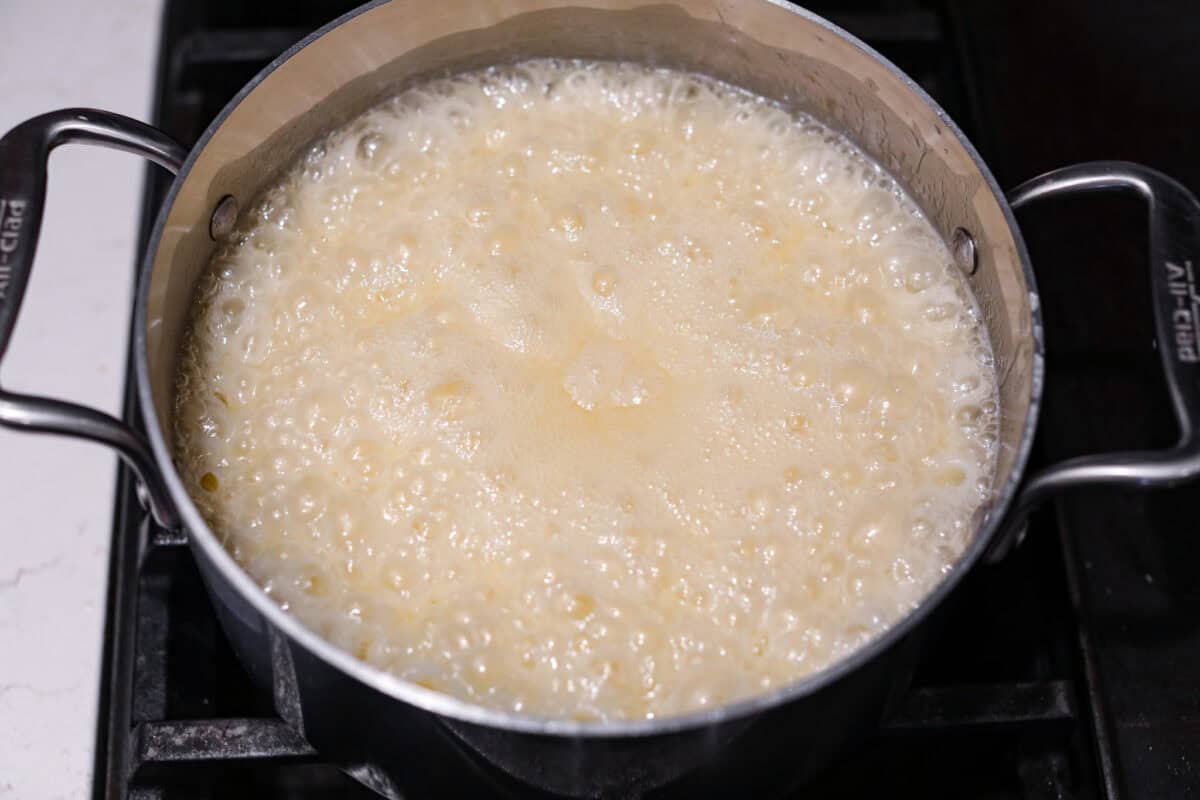 Overhead shot of corn syrup, sugar and butter mixture boiling in a saucepan on the stove. 