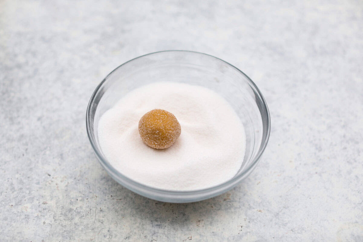 Angle shot of a ball of dough in a bowl of sugar. 