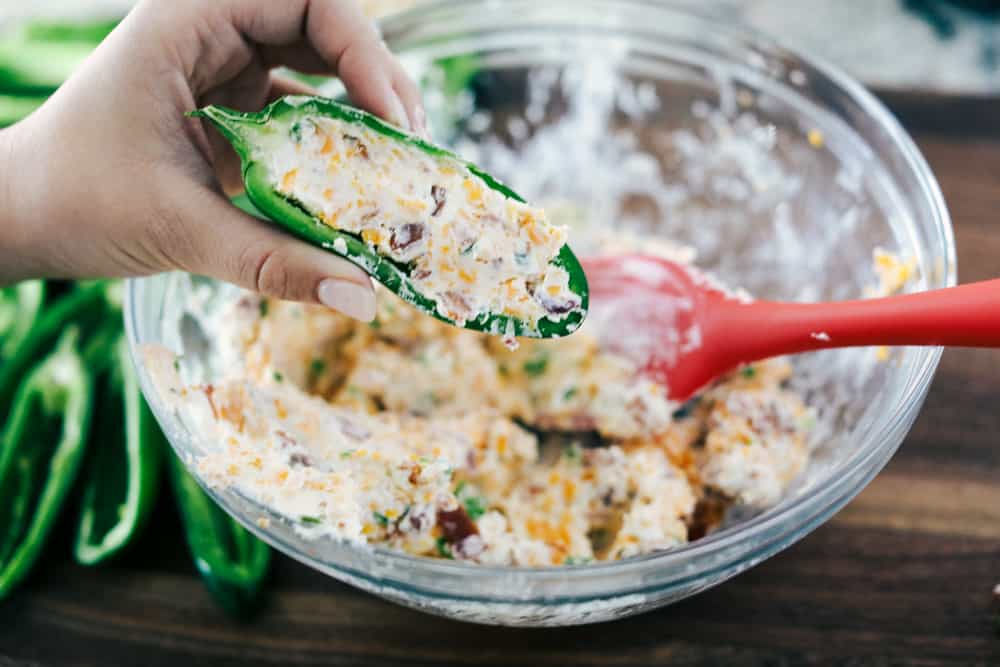 Jalapeño poppers being stuffed with cream cheese, cheese and bacon mixture.