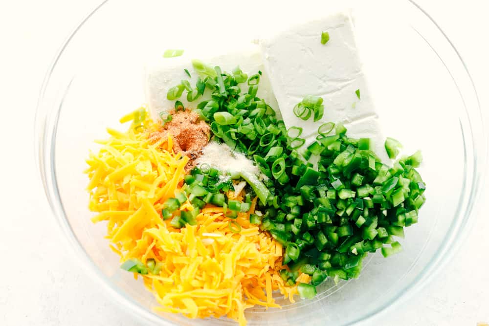 Cheese ball ingredients being added to a glass bowl.